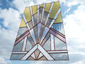 Art Deco 2 Tiffany stained-glass panel in gold, blue and lavender, shown against a cloudy sky.